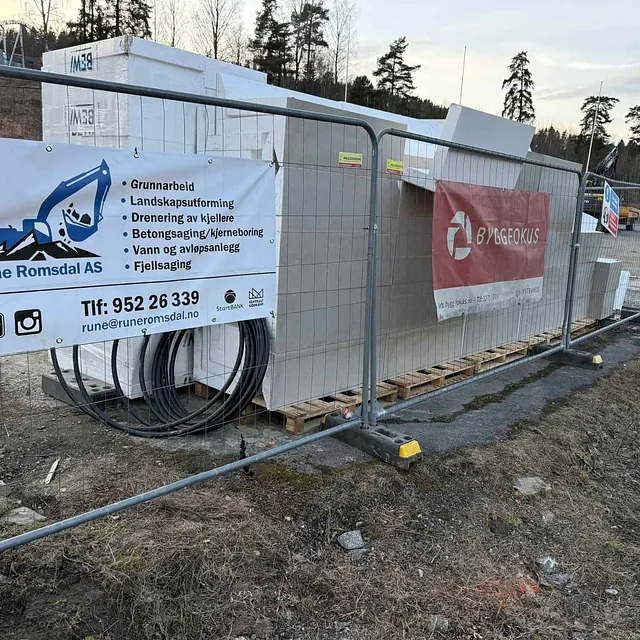 Byggeplass med gjerder, materialer og banner fra Rune Romsdal AS.