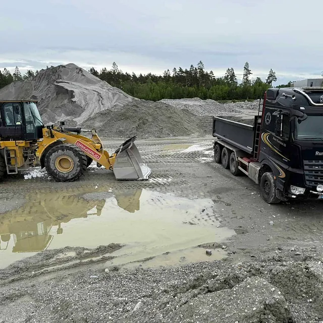 Hjullaster og lastebil står ved grushaug på steinbrudd.