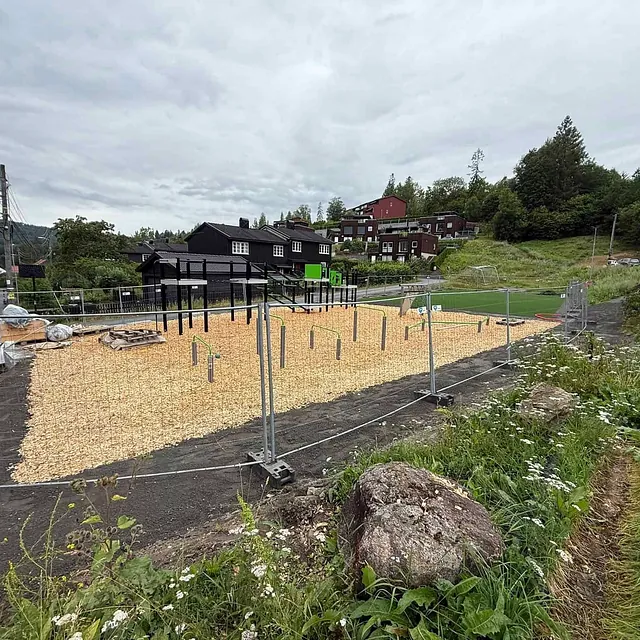 Gjerde rundt nytt lekeområde med barkdekke og monterte stolper.